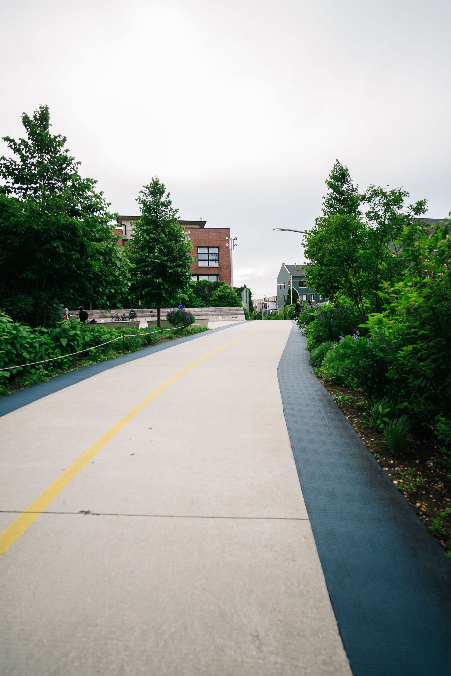 A serene urban walkway surrounded by lush greenery and modern structures on a cloudy day.