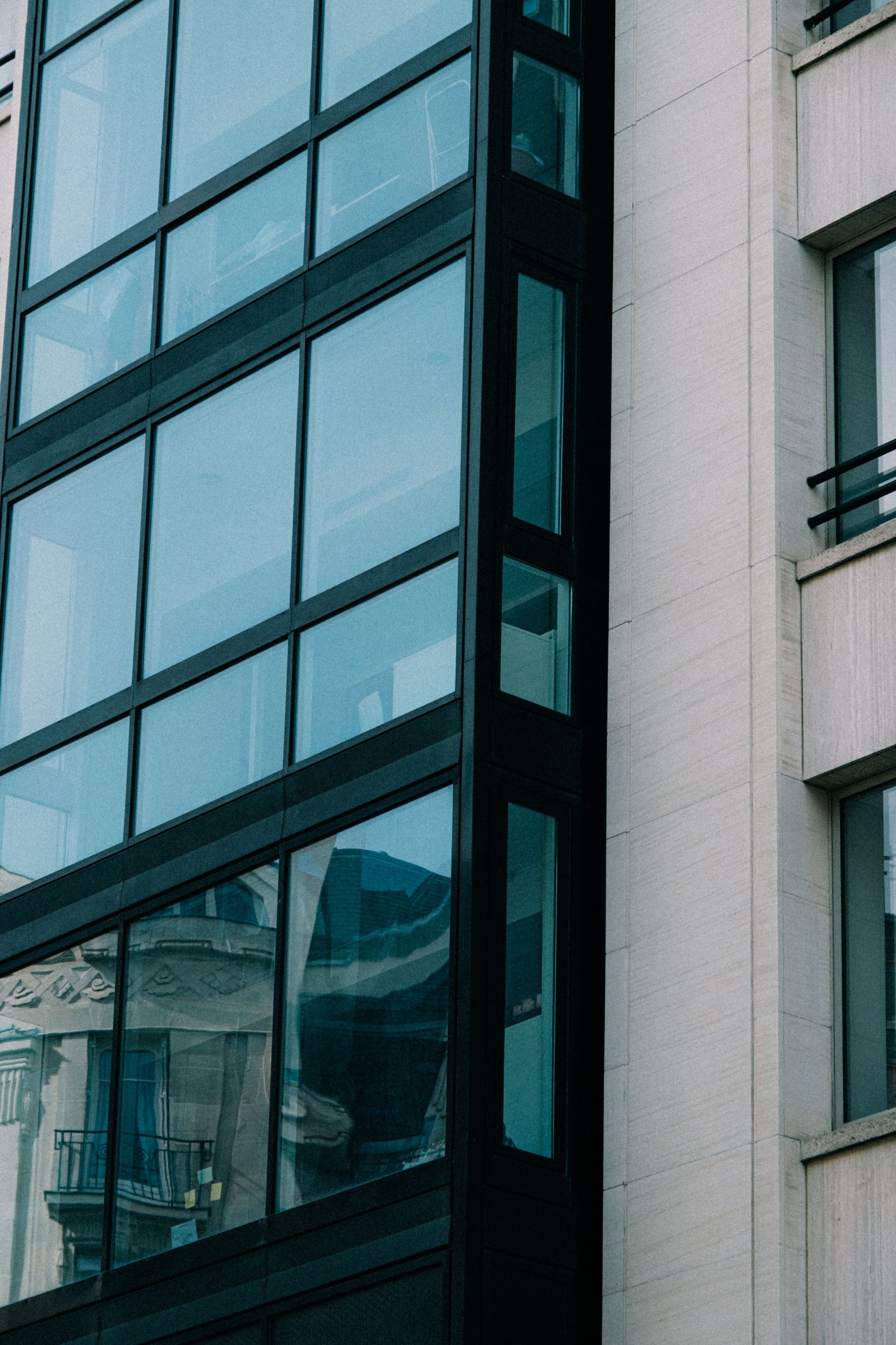 Low angle shot of modern building facade with glass windows reflecting urban surroundings.