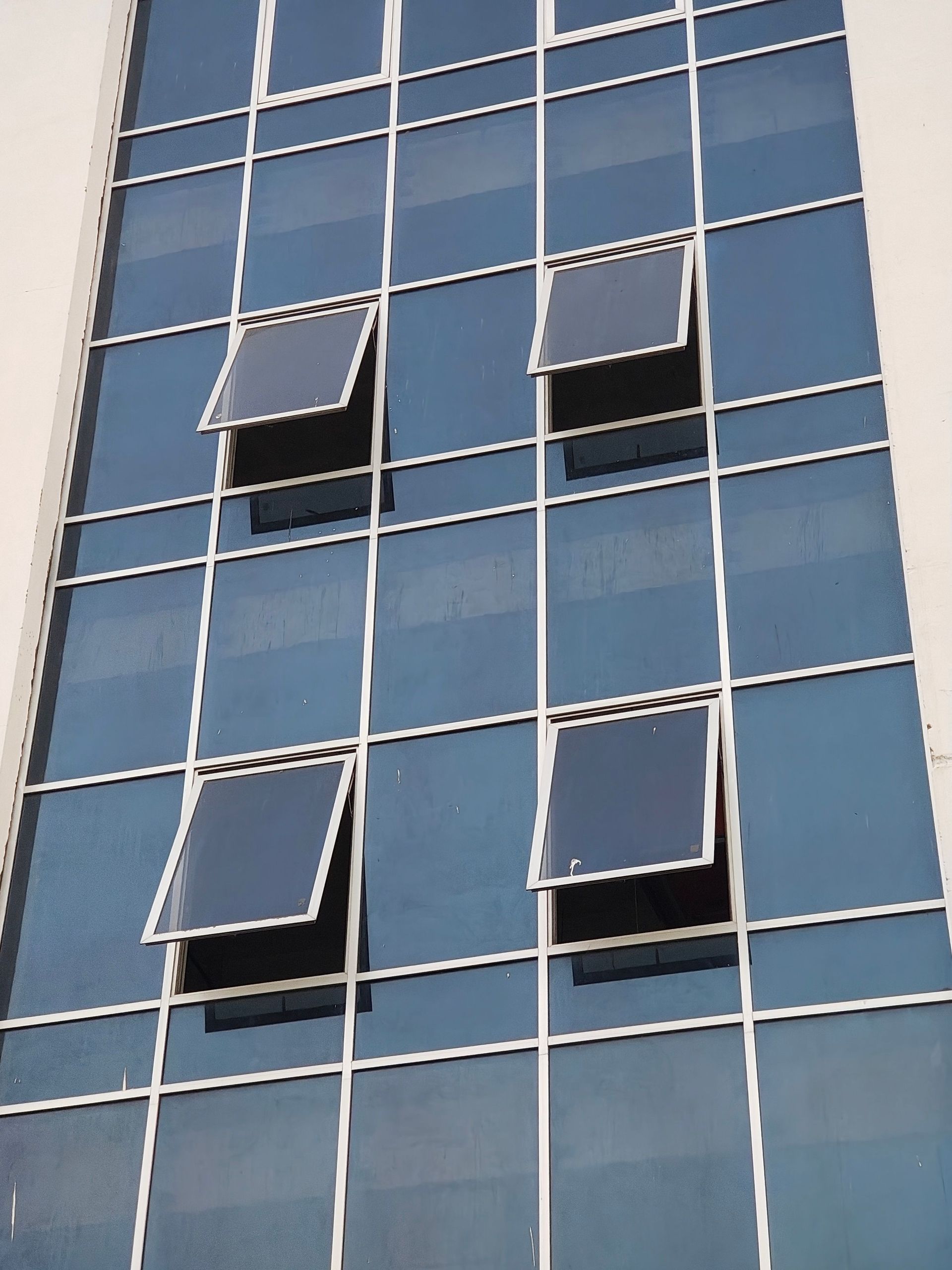 Blue glass building facade with open windows creating an abstract architectural pattern.